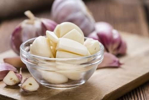 Peeled garlic cloves in a bowl with bulbs behind them