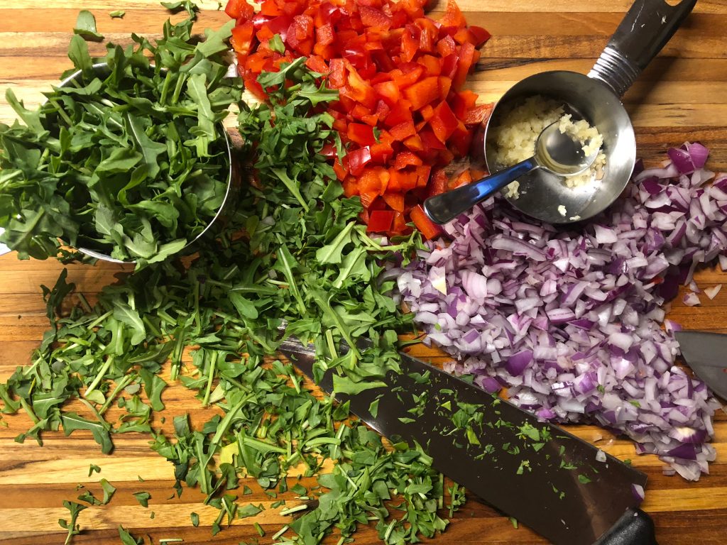 Arugula, red peppers, onions, and garlic on a cutting board