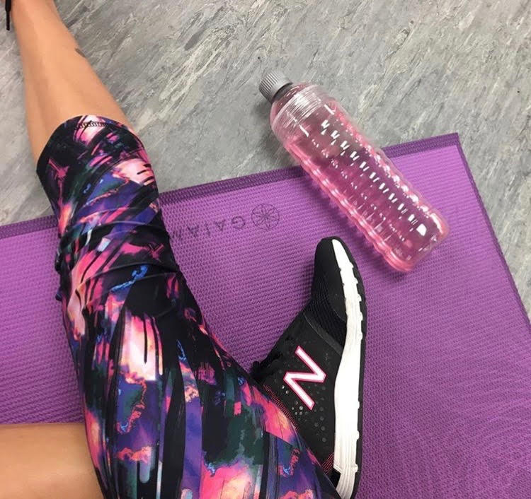 Leg  with leggings on a purple Gaiam yoga mat with a pink drink beside it. 