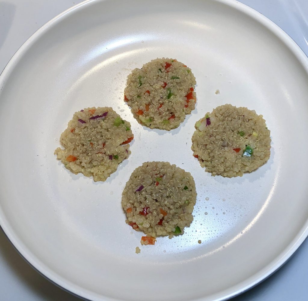 four uncooked quinoa hash brown patties in a skillet
